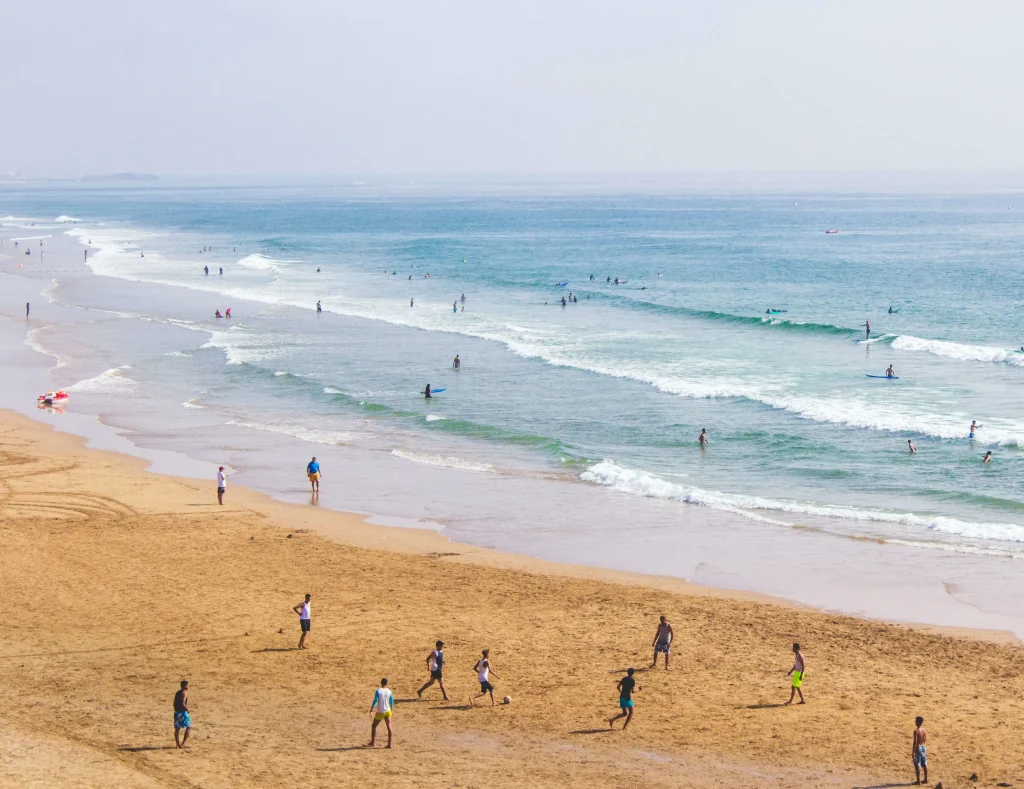 Surfing in Morocco for Beginners: A Local’s Ultimate Guide Taghazout beach full of people surfing and playing football